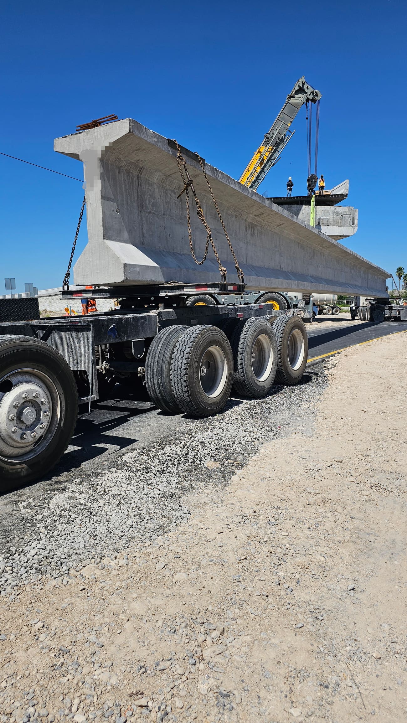 Transporte de una trabe prefabricada de concreto sobre plataforma especializada, con grúa realizando montaje al fondo