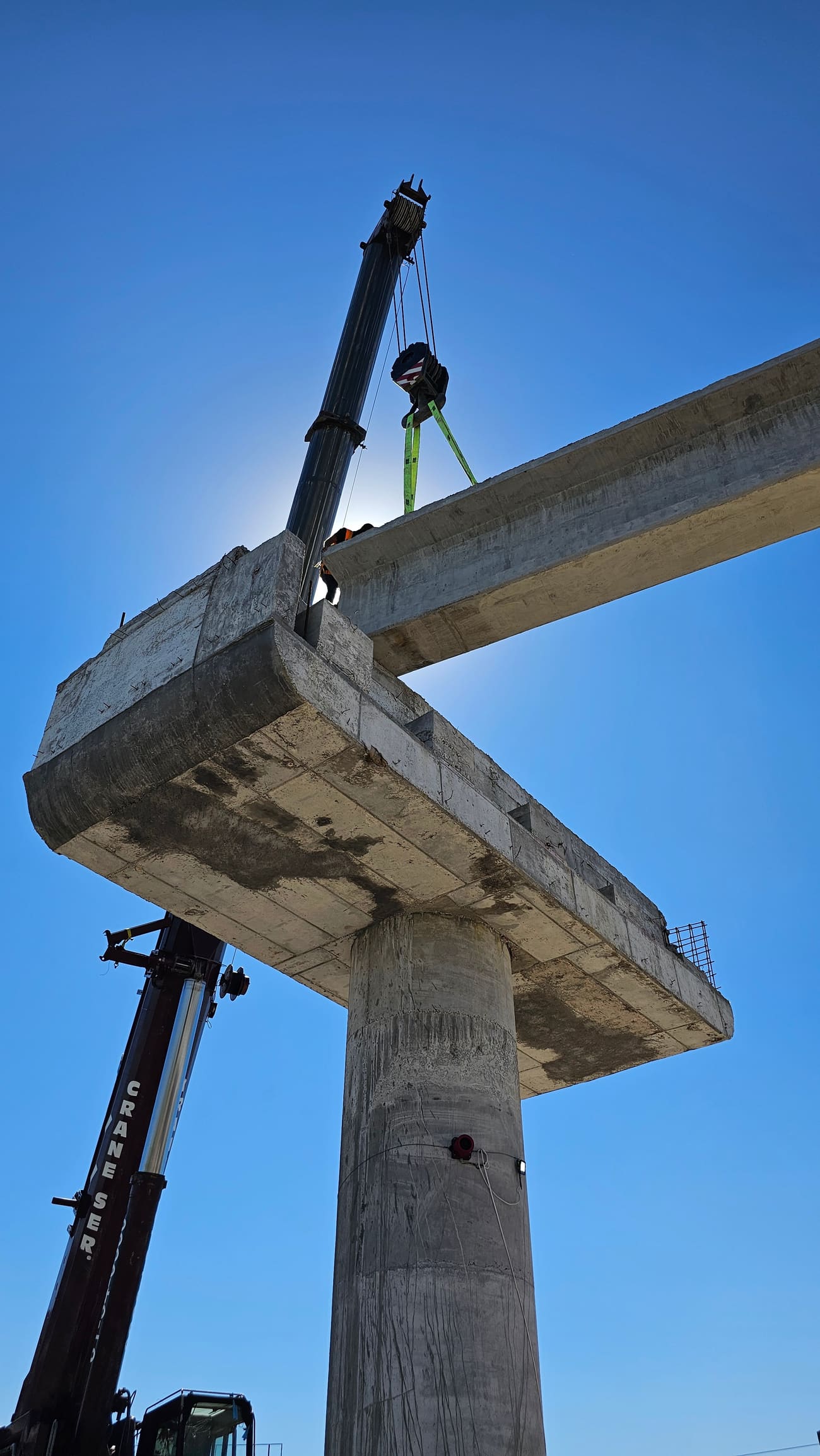 Vista en contrapicado de un elemento prefabricado de concreto siendo colocado por grúa sobre una pila de puente